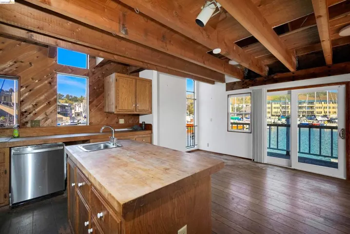 Kitchen with a center island with sink, dishwasher, wood walls, plenty of natural light, and wood finish cabinetry