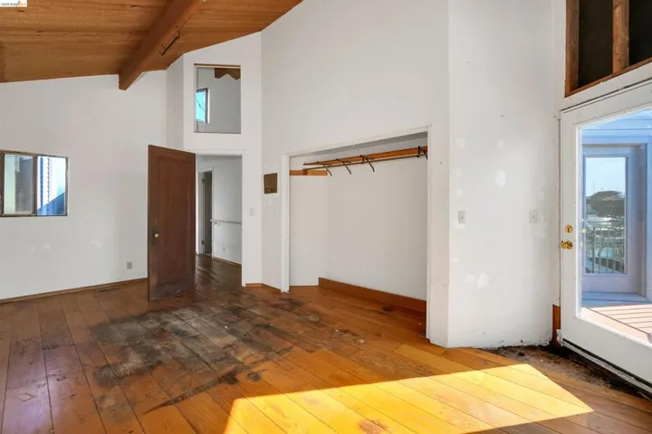 Unfurnished bedroom with wood-type flooring, multiple windows, and a high wood beamed ceiling