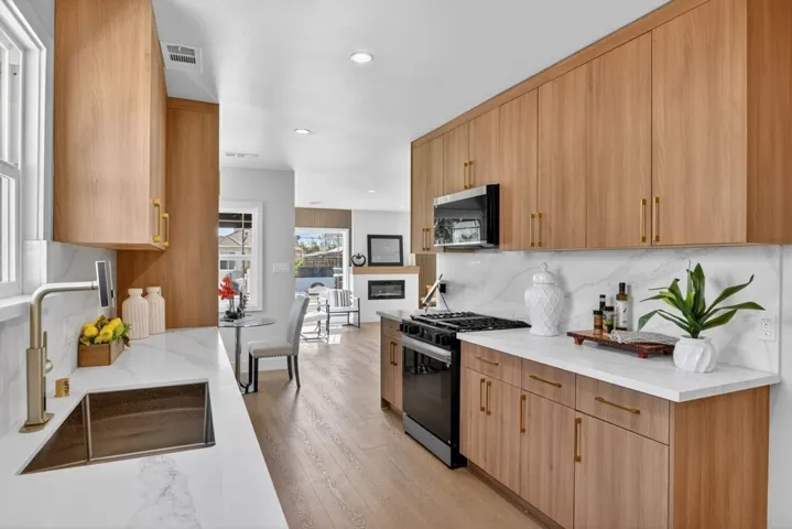 Kitchen featuring black gas stove, light stone counters, light wood-type flooring, stainless steel microwave, and recessed lighting
