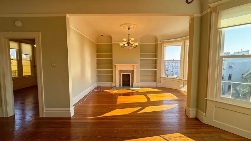 Unfurnished living room with hanging lights, built in shelves, dark wood finished floors, and healthy amount of natural light