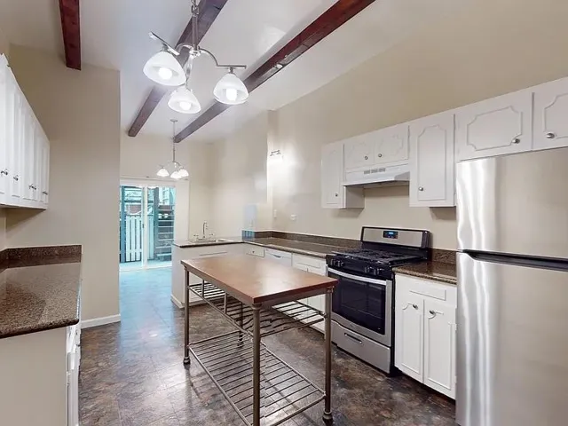 Kitchen featuring appliances with stainless steel finishes, beam ceiling, white cabinets, a chandelier, and under cabinet range hood