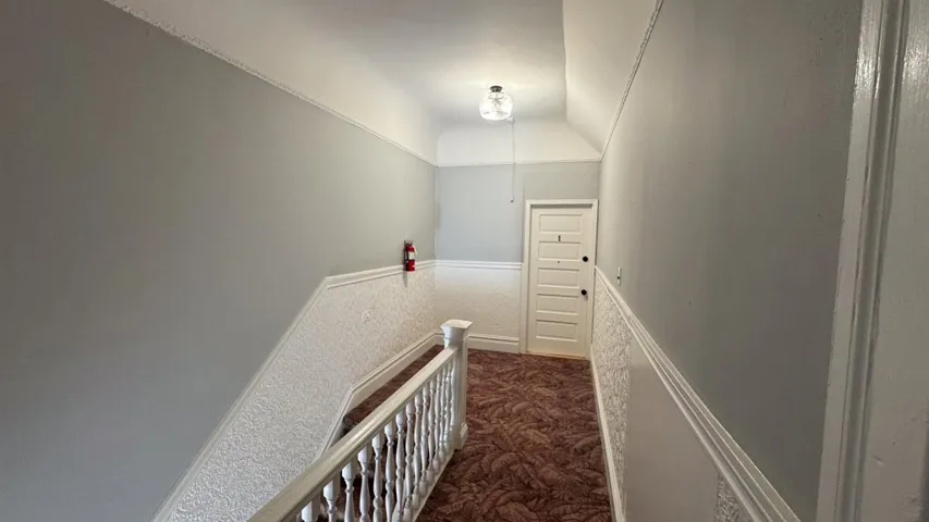 Hall featuring dark colored carpet and an upstairs landing