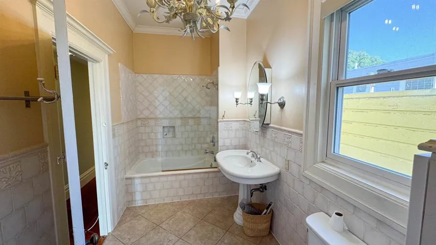 Bathroom with tile walls, a wainscoted wall, tiled shower / bath, crown molding, and tile patterned floors