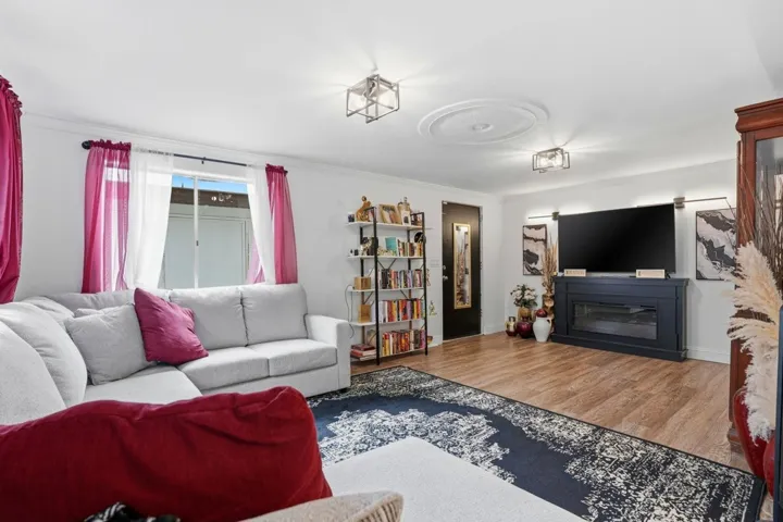 Living room with wood finished floors, a glass covered fireplace, and ornamental molding