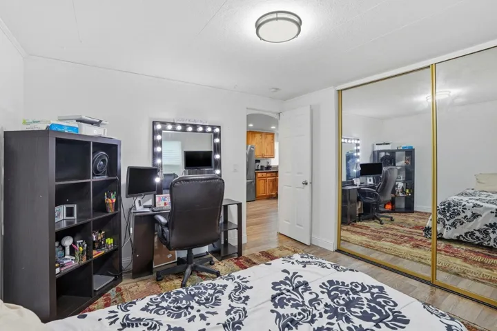 Bedroom with an office area, light wood-style floors, a closet, freestanding refrigerator, and arched walkways