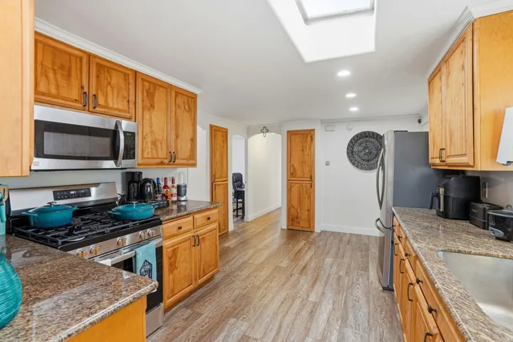 Kitchen with stainless steel appliances, recessed lighting, dark stone counters, light wood finished floors, and a skylight