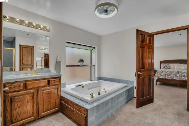 Ensuite bathroom featuring vanity, light carpet, a whirlpool tub, and ceiling fan