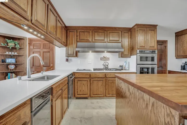 Kitchen featuring wood finish cabinetry, butcher block counters, stainless steel appliances, light marble finish flooring, and open shelves