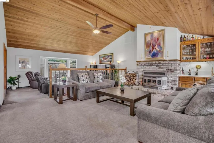 Living area featuring light colored carpet, a high wooden beamed ceiling, ceiling fan, and a brick fireplace