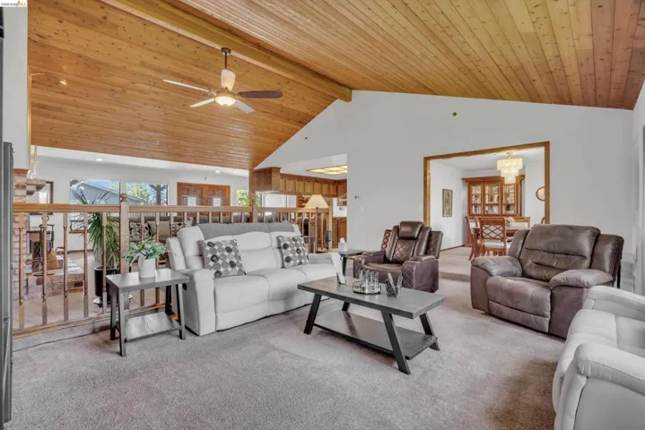 Carpeted living room with a high wood beamed ceiling and ceiling fan