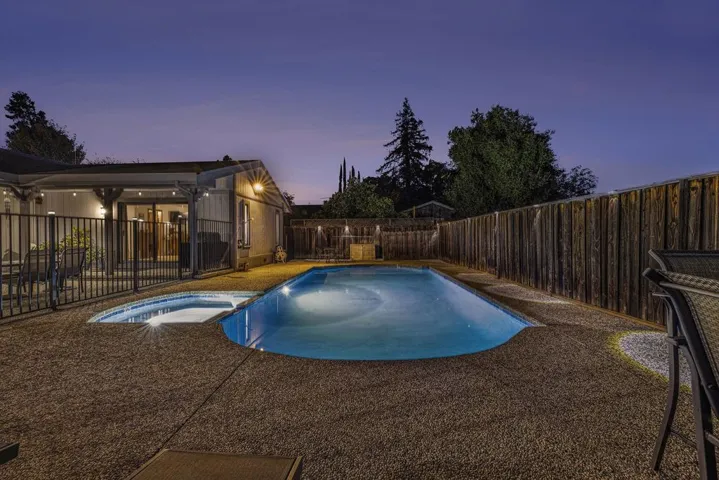 Pool at dusk featuring a fenced backyard, a patio, and a pool with connected hot tub