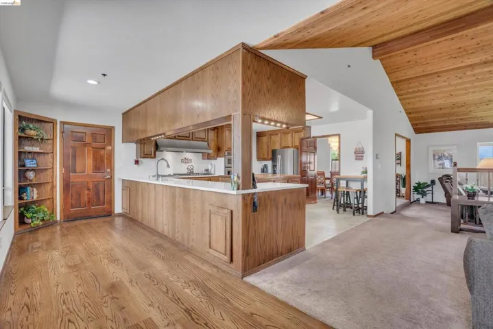 Kitchen featuring light countertops, a peninsula, open floor plan, wood finish cabinets, and stainless steel fridge with ice dispenser