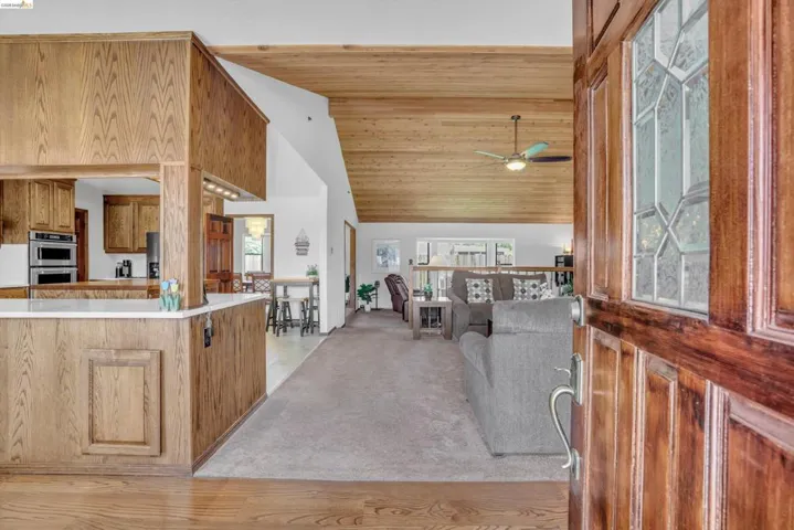 Living area featuring a vaulted wooden ceiling, light colored carpet, and ceiling fan