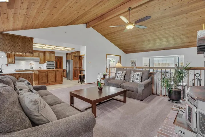 Living room featuring light colored carpet, a ceiling fan, and a high wooden beamed ceiling