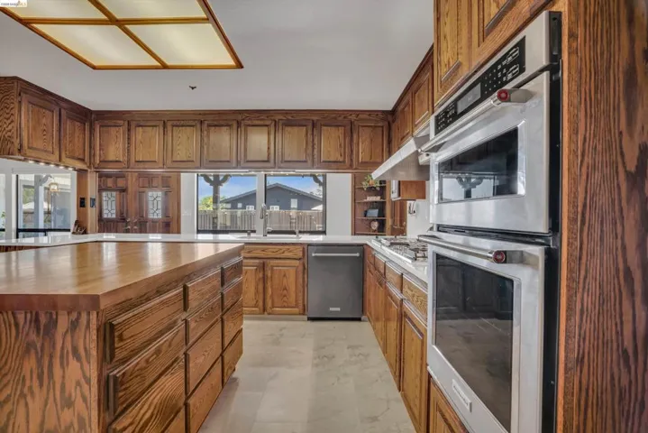 Kitchen with wooden counters, stainless steel appliances, wood finish cabinetry, a center island, and light marble finish floors