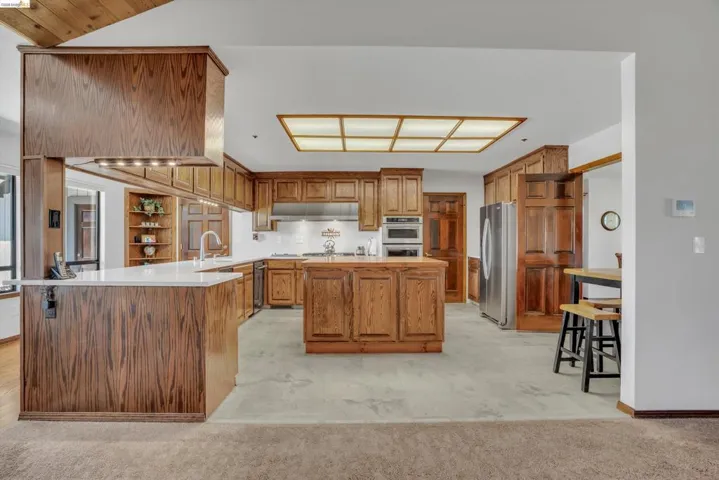 Kitchen with wood finish cabinets, light countertops, a center island, a peninsula, and stainless steel appliances
