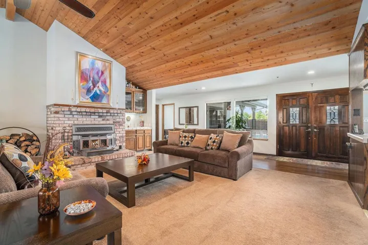 Living area featuring wood ceiling, a brick fireplace, high vaulted ceiling, light wood-style flooring, and ceiling fan