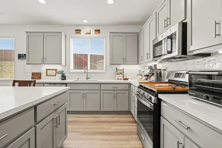 Kitchen featuring gray cabinetry, stainless steel appliances, light wood finished floors, recessed lighting, and tasteful backsplash