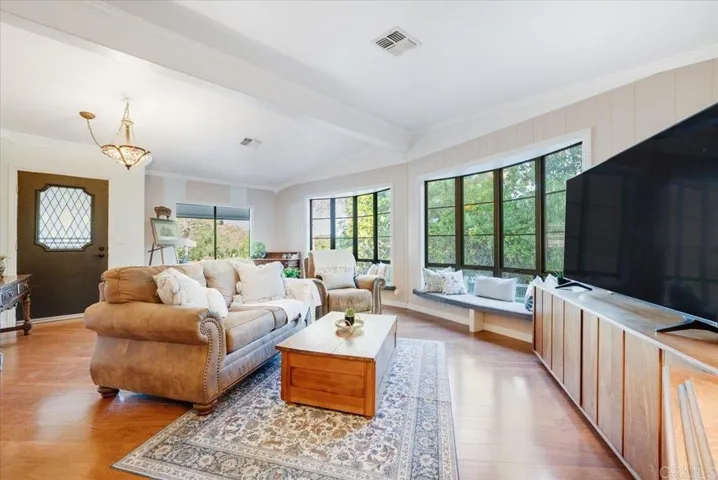 Spacious living area with warm wood floors, large windows, and comfortable seating.