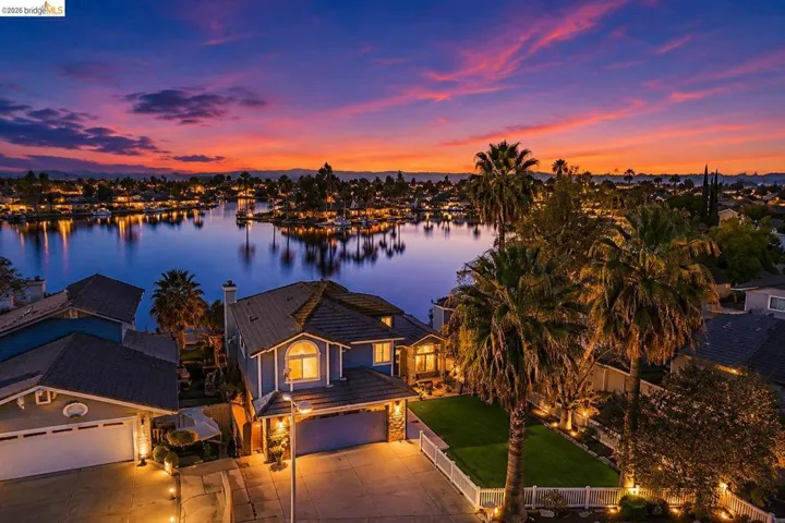 Waterfront residence featuring a private boat dock, mature palm trees, an attached two-car garage, and a manicured lawn with a white picket fence