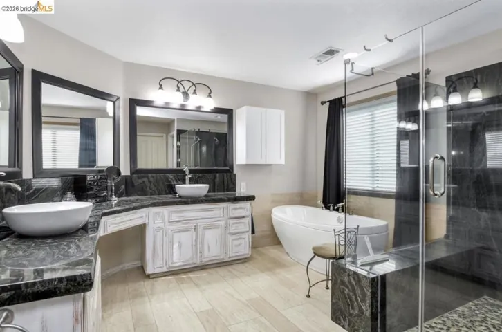 Bathroom with a shower stall, double vanity, a freestanding tub, tile walls, and a wainscoted wall