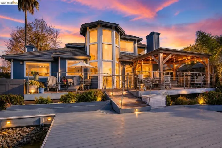 Waterfront residence with a multi-level decking system, featuring a cable railing system, a covered patio with exposed wood beams, and an architectural glass window tower