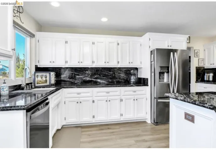 Kitchen featuring dark stone countertops, stainless steel appliances, white cabinetry, light wood-style floors, and recessed lighting