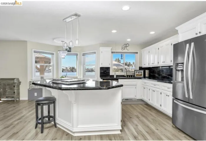 Kitchen with stainless steel appliances, hanging light fixtures, dark stone countertops, a breakfast bar area, and white cabinets