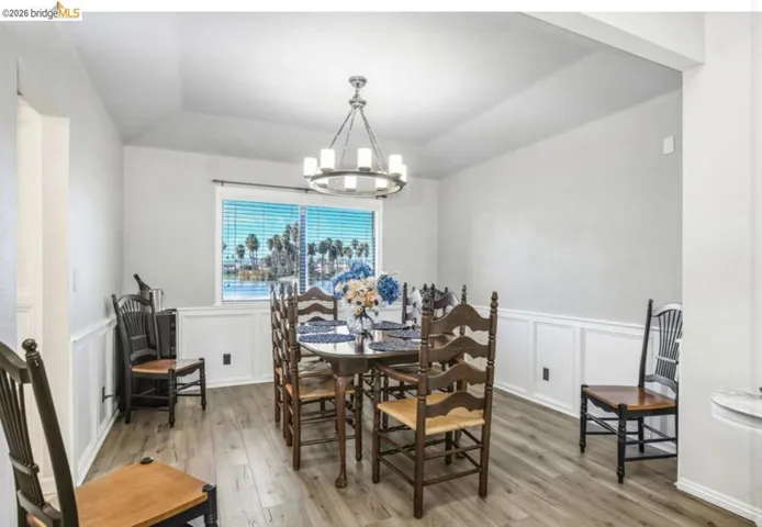 Dining space with light wood finished floors, a decorative wall, a chandelier, vaulted ceiling, and a wainscoted wall