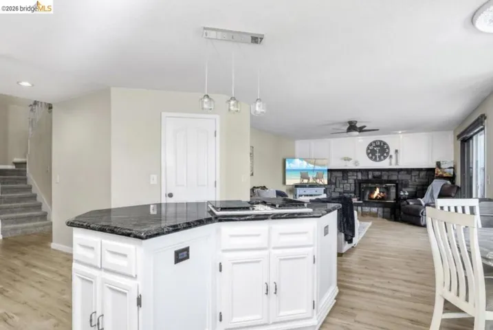 Kitchen with white cabinets, hanging light fixtures, open floor plan, ceiling fan, and a stone fireplace