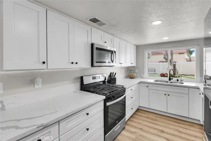 NEWER STAINLESS STEEL APPLIANCES AND VIEW TO LARGE GRASSY BACKYARD.