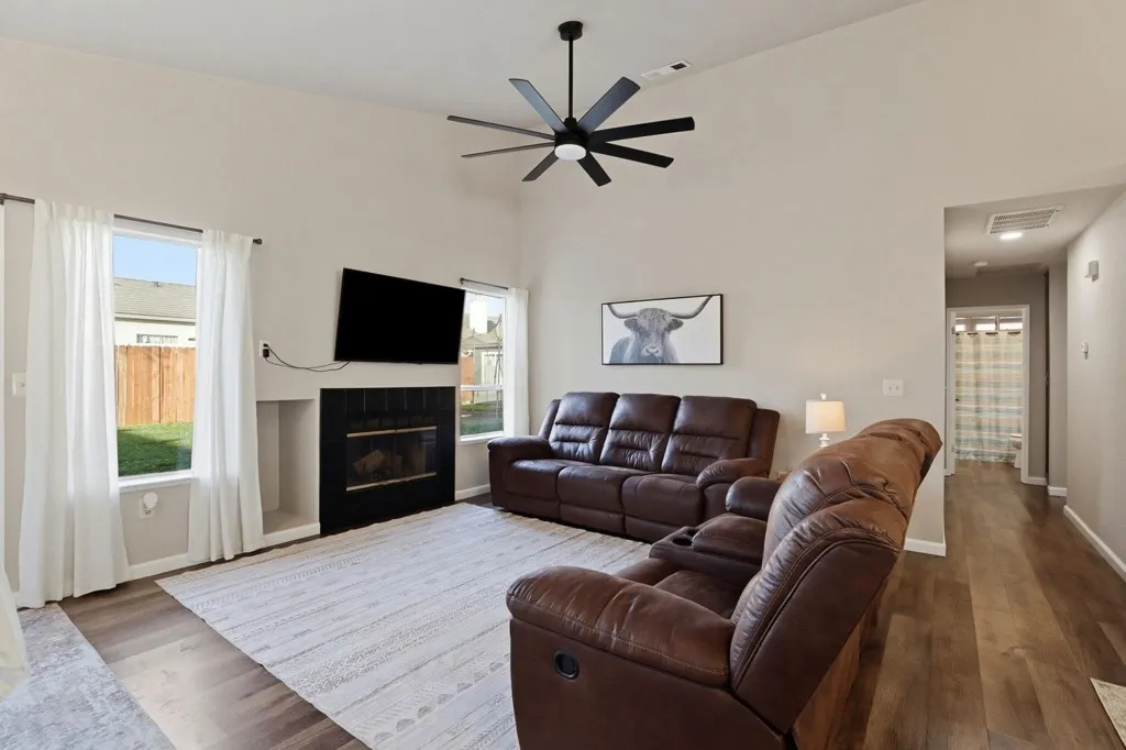 Living area with a fireplace, wood finished floors, ceiling fan, plenty of natural light, and a high ceiling