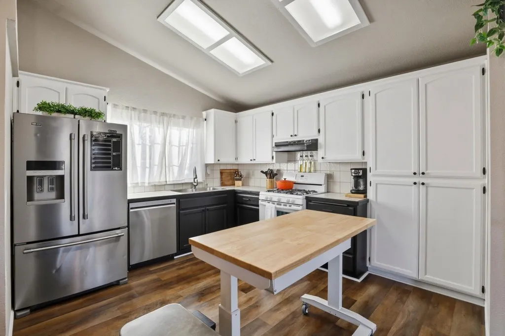 Dual tone kitchen with stainless steel appliances, backsplash, dark wood-type flooring, vaulted ceiling, and two tone cabinets