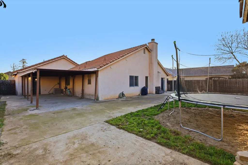 View of side of home with a fenced backyard, a trampoline, stucco siding, and a chimney