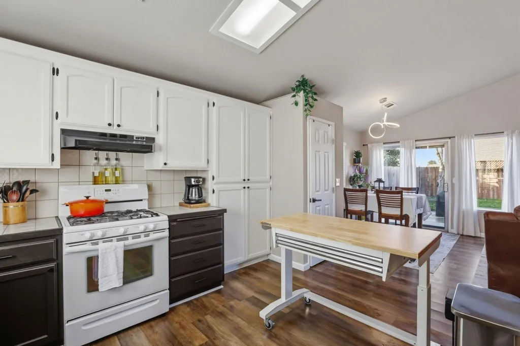 Kitchen featuring white range with gas cooktop, dual tone cabinets, tile countertops, tasteful backsplash, and lofted ceiling