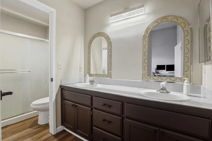 Bathroom with double vanity, a textured wall, and dark wood-style flooring
