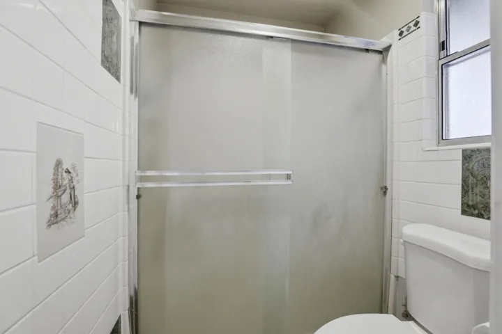 Full bathroom featuring a shower stall and tile walls