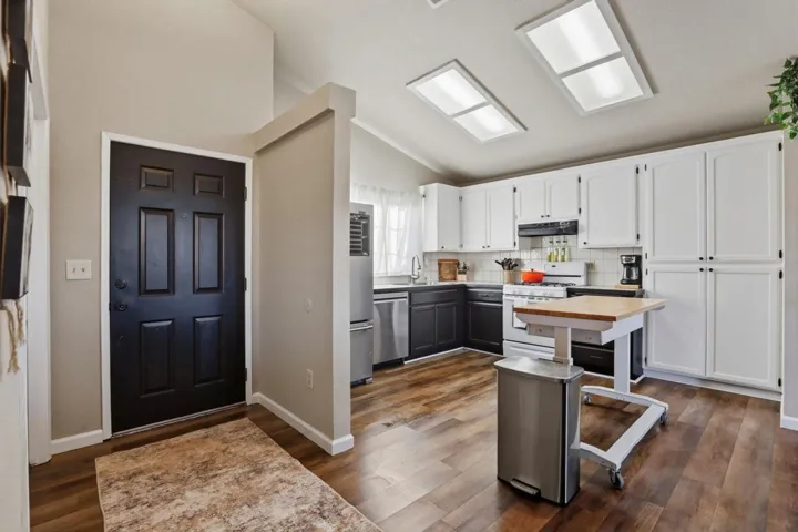 Kitchen with vaulted ceiling, stainless steel appliances, tasteful backsplash, dark wood-style flooring, and two tone cabinetry