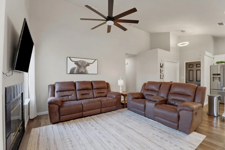 Living area featuring a glass covered fireplace, wood finished floors, vaulted ceiling, and a ceiling fan
