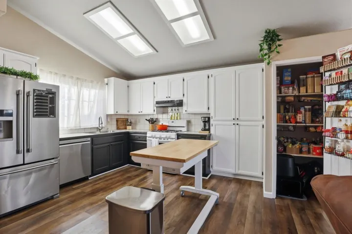Dual tone kitchen with stainless steel appliances, two tone cabinetry, dark wood-style flooring, tasteful backsplash, and lofted ceiling