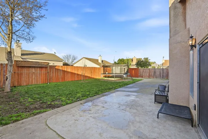 Fenced backyard featuring a trampoline and a patio area