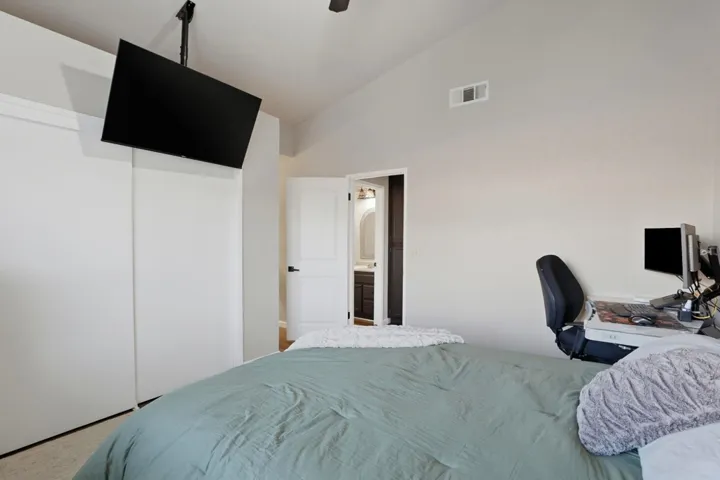 Carpeted bedroom featuring vaulted ceiling, a ceiling fan, a desk, ensuite bath, and a closet