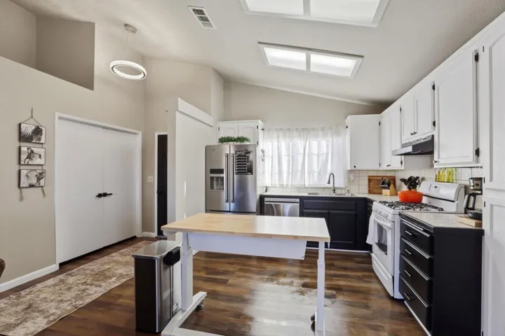Dual tone kitchen featuring stainless steel appliances, two tone cabinetry, light countertops, lofted ceiling, and tasteful backsplash