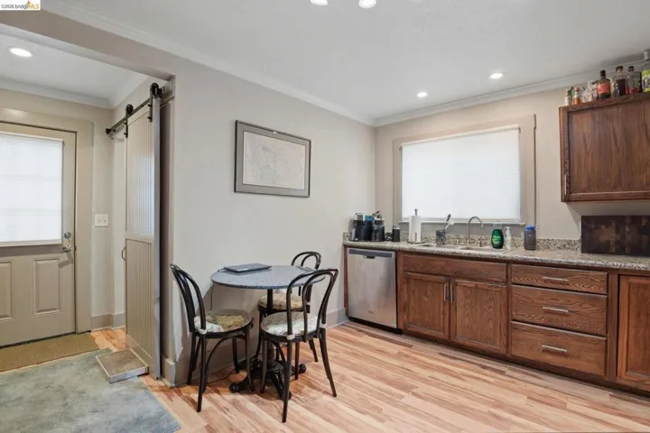 Kitchen featuring a barn door, stainless steel dishwasher, light wood-style flooring, recessed lighting, and crown molding