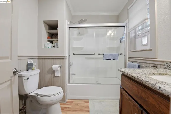 Full bath featuring vanity, crown molding, light wood-style floors, built in shelves, and combined bath / shower with glass door