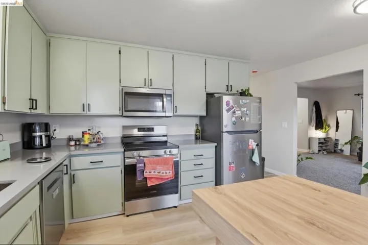 Kitchen with stainless steel appliances, light wood-style floors, and green cabinetry