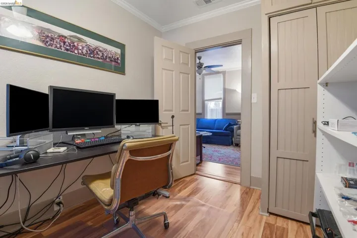 Home office with light wood-style flooring, crown molding, and a ceiling fan