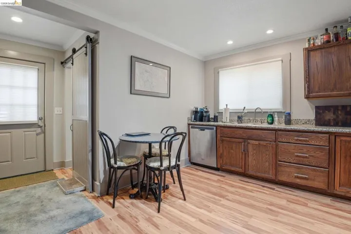 Kitchen with a barn door, stainless steel dishwasher, crown molding, light wood-style floors, and recessed lighting