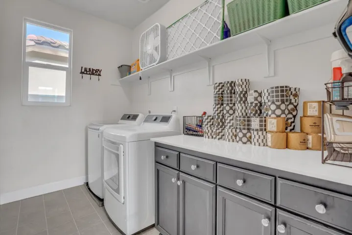 Laundry area with separate washer and dryer, light tile patterned flooring, and cabinet space