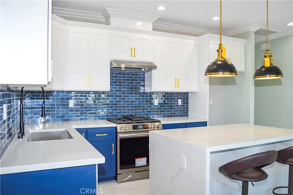 Unit 2 - Well-appointed kitchen with range, hood, dishwasher, quartz counters, waterfall edge on island, and custom lighting